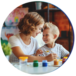 Mom painting with green, blue, yellow, and red paint with her young son at the kitchen table