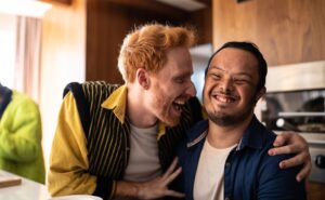 Two individuals laughing while sitting at a table in a kitchen.