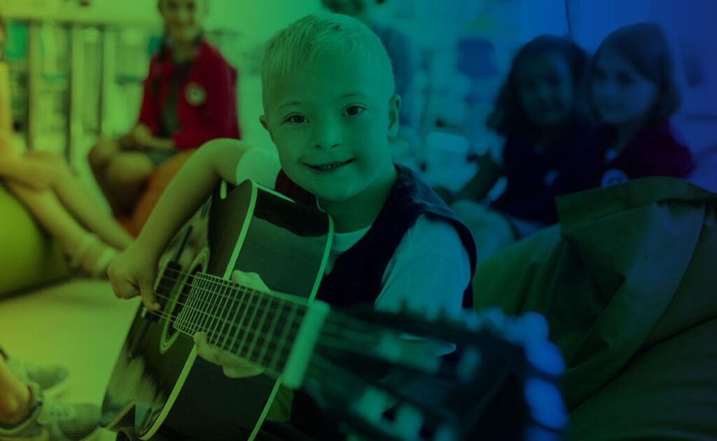 a boy with down syndrome playing an acoustic guitar in a classroom